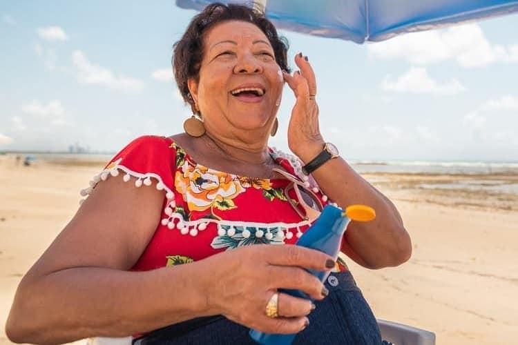 Photo of a woman sitting under an umbrella on the beach applying sunscreen