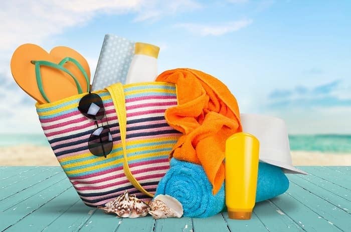Photo of a colorful tote bag containing sunscreen, sunglasses, a hat, towels, and shoes.