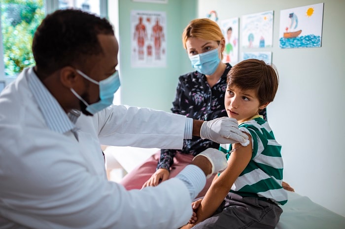 Photo of a doctor giving a young boy a flu shot while his mother looks on