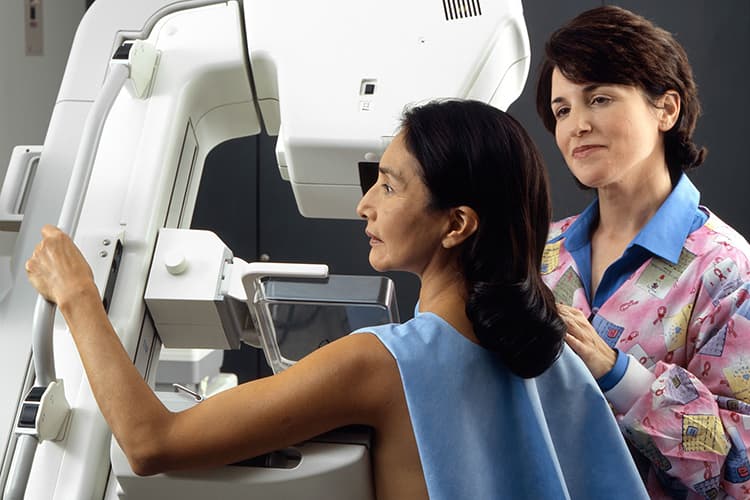 A technician positions a Hispanic woman at an imaging machine to receive a mammogram