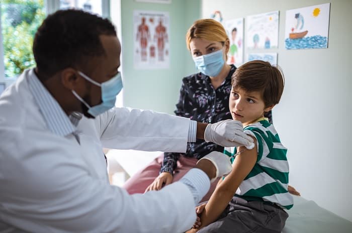 Photo of a doctor giving an HPV vaccine to a boy while his mother looks on