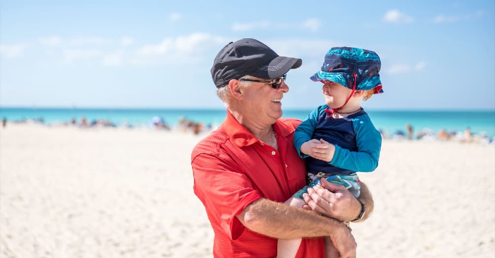 Photo of a grandfather on the beach holding his young grandson