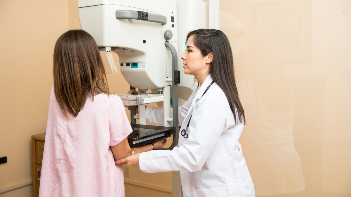 Healthcare professional positioning a woman for a mammogram.