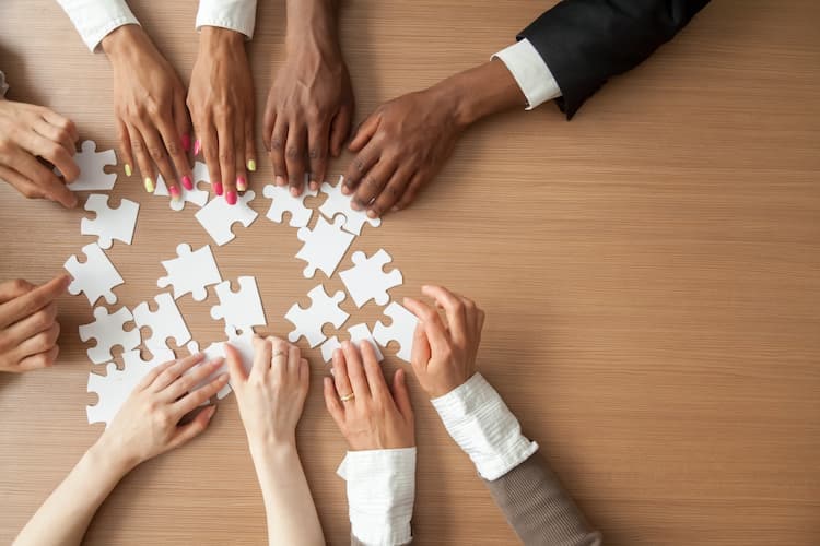 Hands of multi-ethnic business team assembling jigsaw puzzle, top view royalty-free stock photo.
