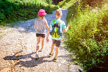 Photo of a boy and a girl walking in a mountain trail.