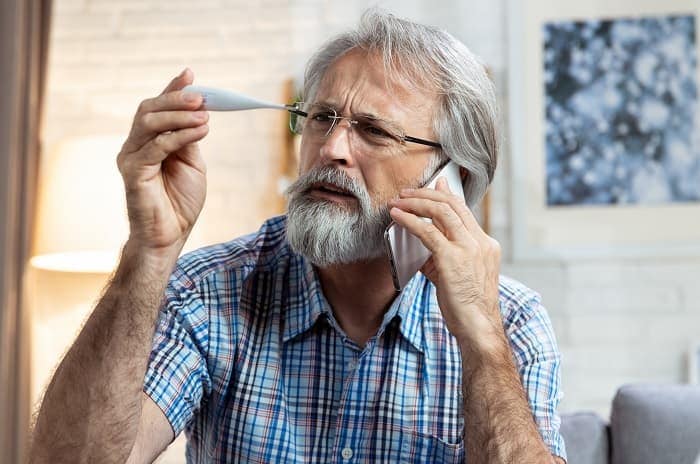 Photo of a man looking at a thermometer and calling his doctor