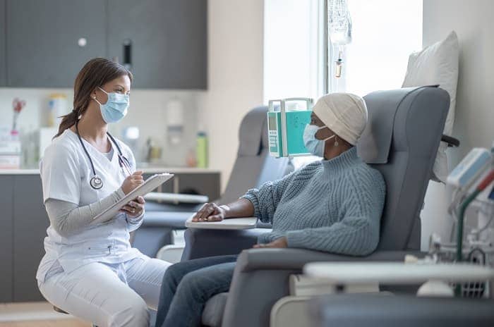Una enfermera se sienta con un paciente de cáncer mayor mientras recibe quimioterapia.
