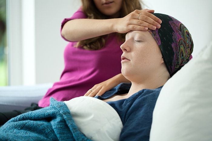 Cuidadora poniendo su mano en la cabeza de una paciente de cáncer que tiene fiebre.