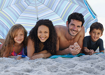 Foto de una pareja con sus hijos en la playa cubriéndose con una sombrilla