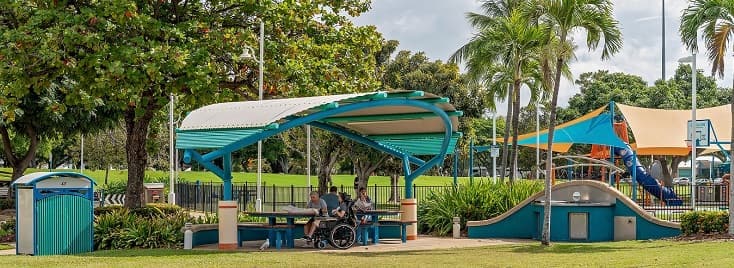 Photo of people enjoying an outdoor picnic under a shade structure near a playground in Australia