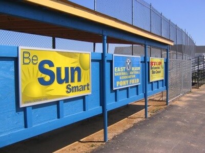 Photo of a shade structure for a school athletic field. Signs on the structure say Be Sun Smart, East Meadow Association Pony Field, and Stop Melanoma Skin Cancer.