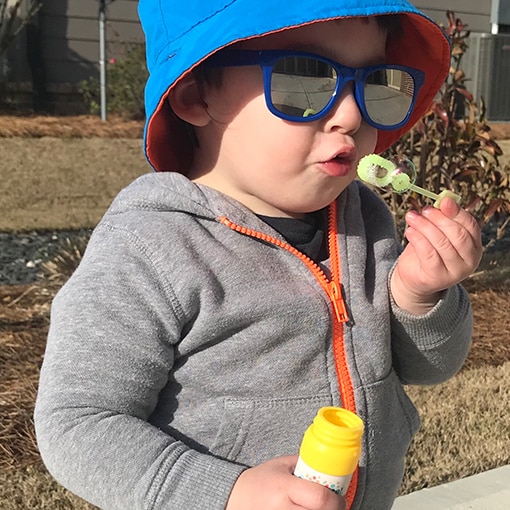 Child wearing sun protection gear and blowing bubbles.