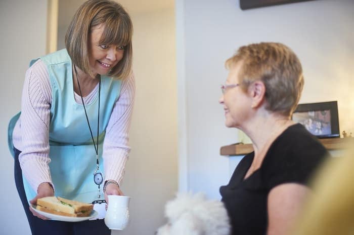 Foto de una asistente de salud en el hogar trayendo almuerzo a una sobreviviente de cáncer en su hogar