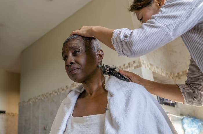 Foto de una mujer afeitando el cabello de un paciente con cáncer que está recibiendo quimioterapia