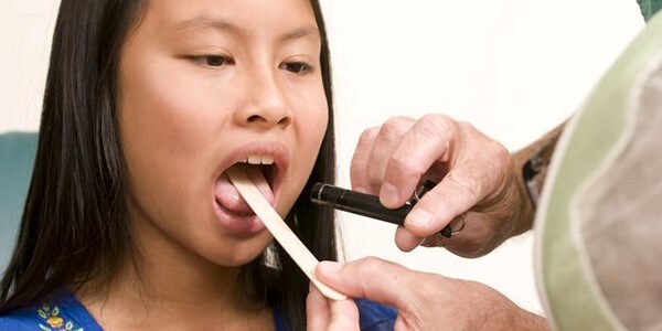 Image of a young girl getting her throat examined by a healthcare professional