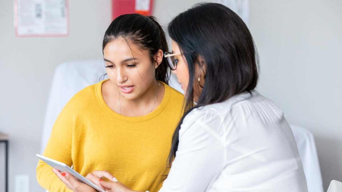 A young woman consults with her doctor, who is showing her information on a tablet.