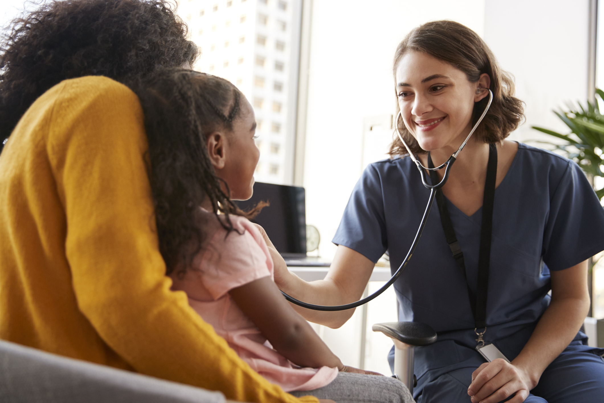 Pediatrician using stethoscope on girl on mom's lap.