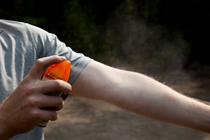 A man is spraying bug spray on his arm.