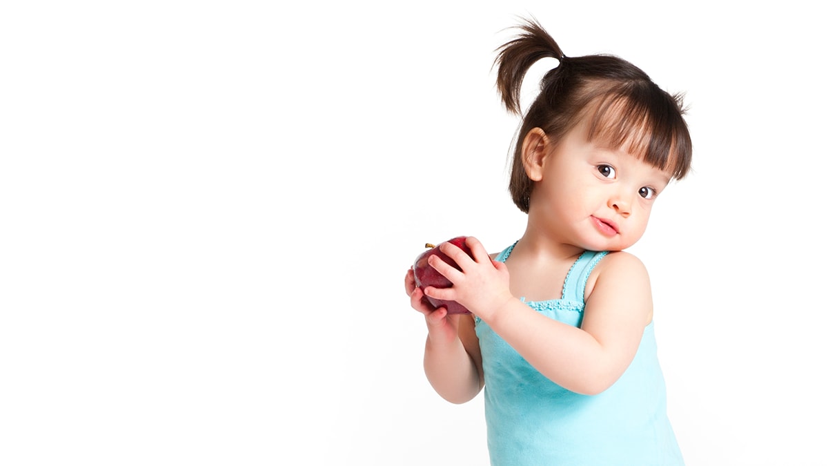 A toddler girl with pigtails holding an apple