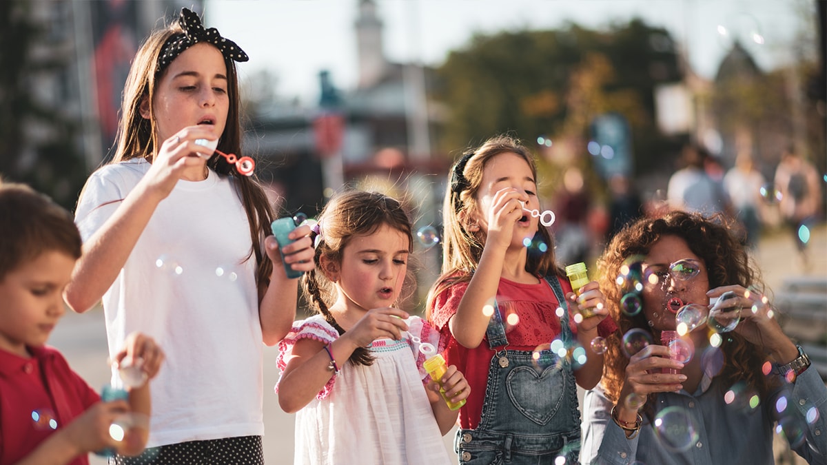 A group of young children and one mother blowing bubbles