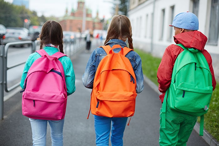 Tres chicas con mochilas caminando a la escuela.