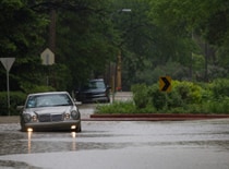 Photo of car driving on a flooded street.