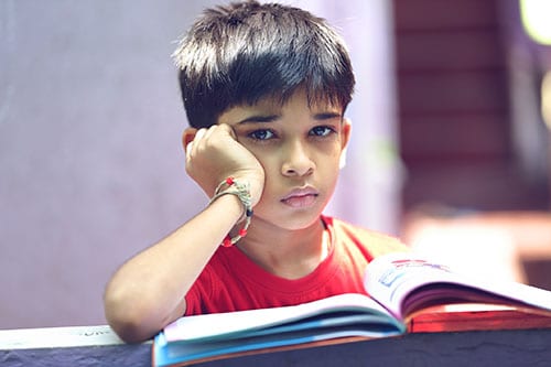 Young boy looking up from a book with a sad face