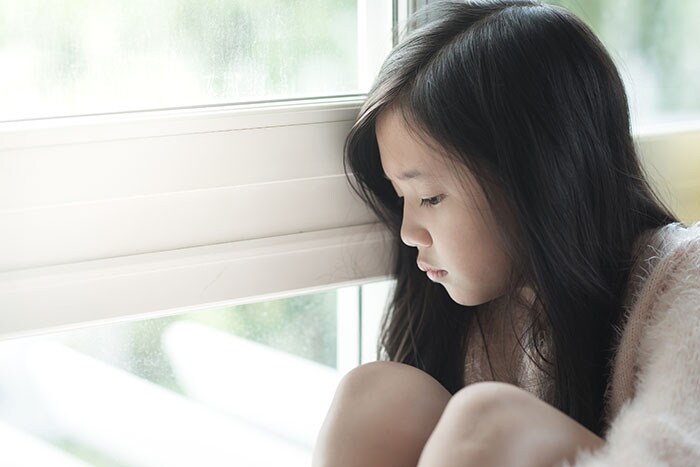 Portrait of sad Asian girl sitting in a window sill