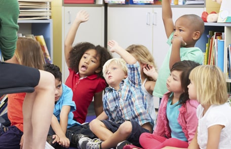 Photo of a group of preschoolers raising their hands in a classroom 