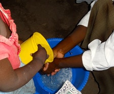 Person washing hands over a bucket of water