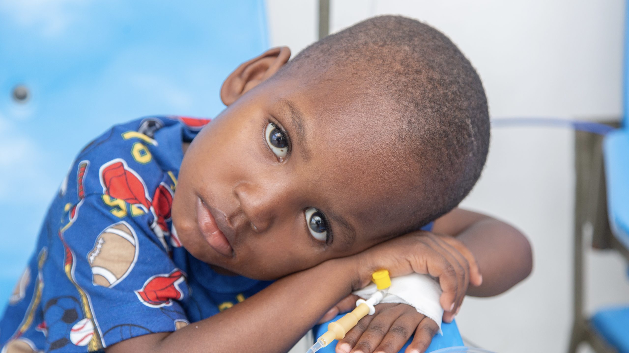 Young boy with his head resting on his crossed arms and being treated for cholera through an IV