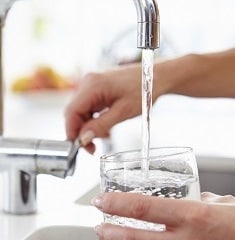 A woman pouring herself a glass of water from faucet. 