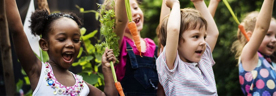 Group of children cheering with fresh carrots in their hands
