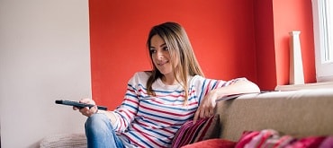 young woman sitting on couch with remote control in hand