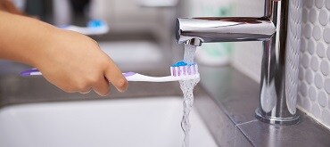 child with toothbrush under water faucet
