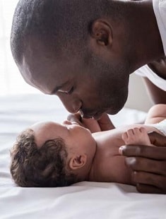 man laying baby on bed on back