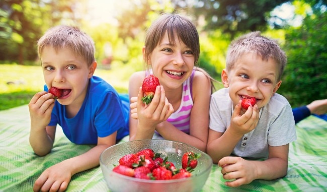 3 children laughing and eating strawberries
