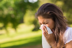 A woman outside blowing her nose into a tissue.