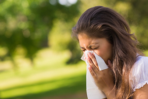 A woman outside blowing her nose into a tissue.