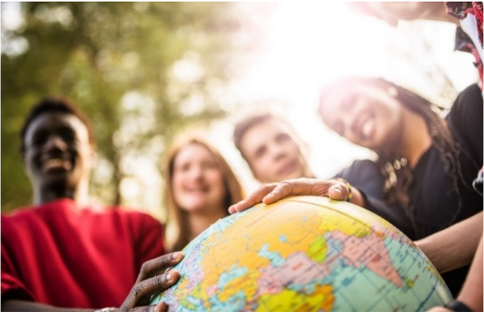 Diverse people smiling with hands placed around a globe