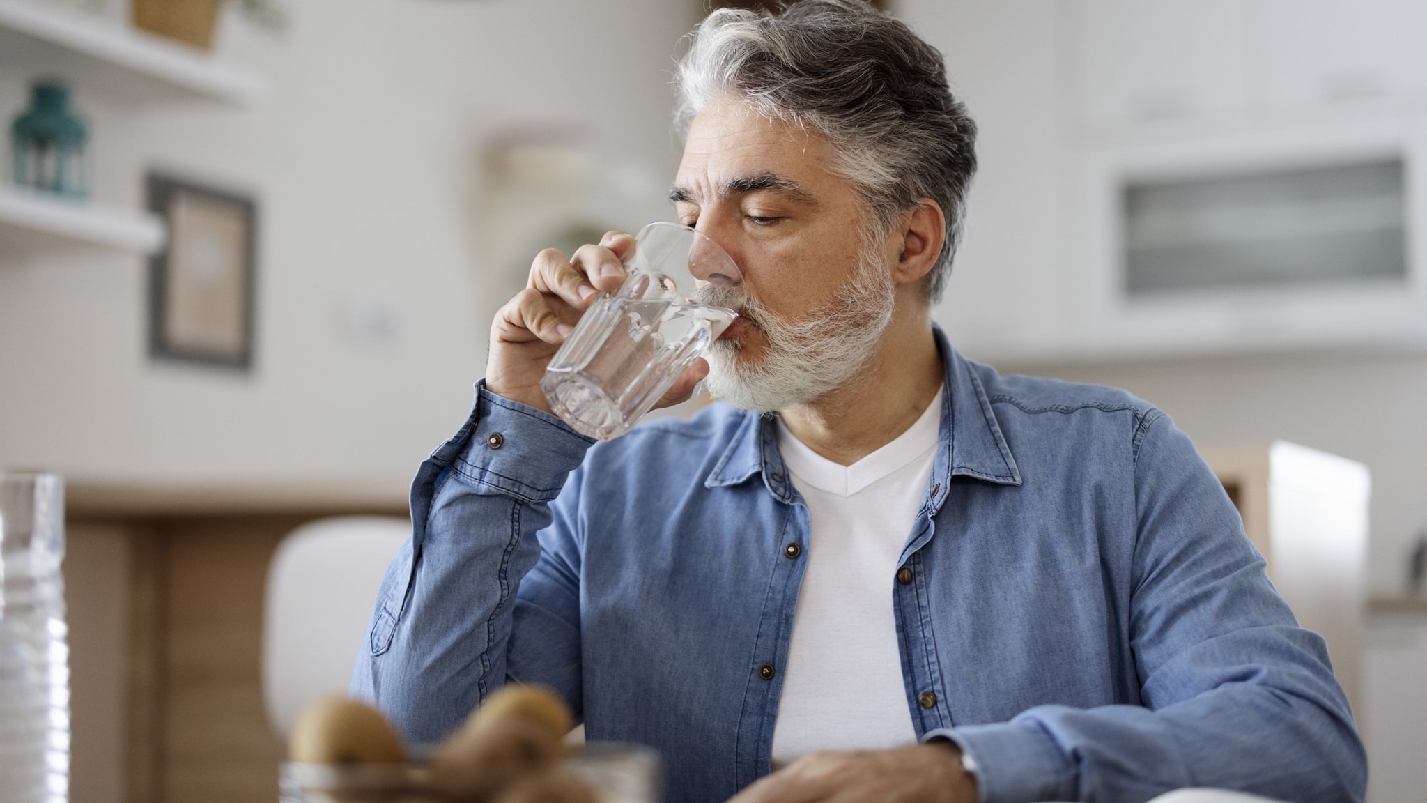An older adult drinking a glass of water sitting down indoors.