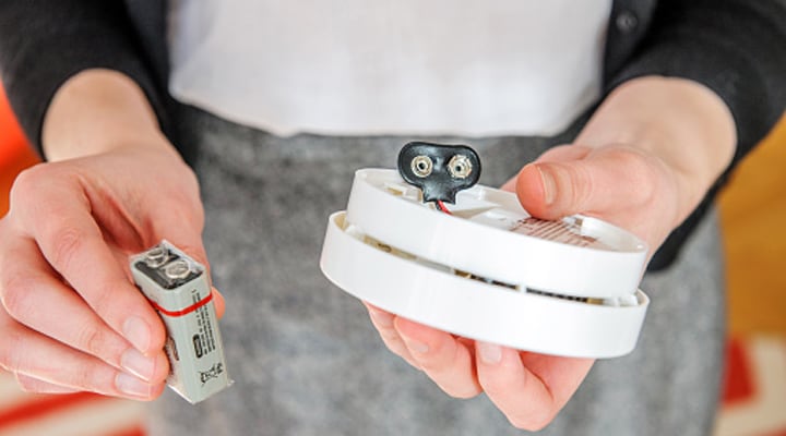a battery in one hand, and a CO detector in the other