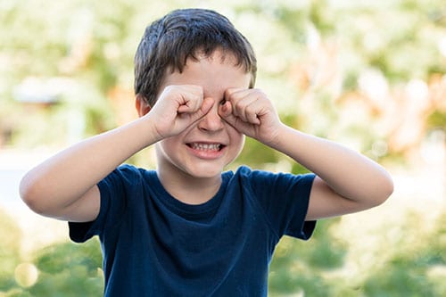 A child outdoors with itching eyes because of pink eye.