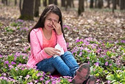 Girl with itchy eyes sitting among flowers