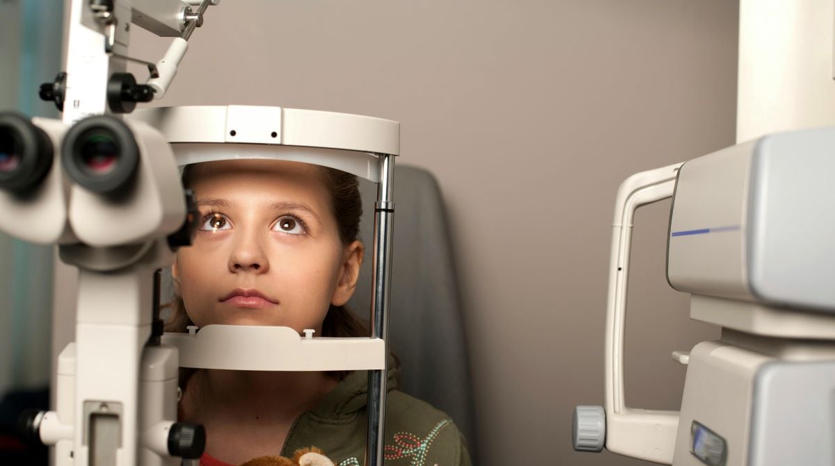 Child patient sitting by eye clinic equipment.