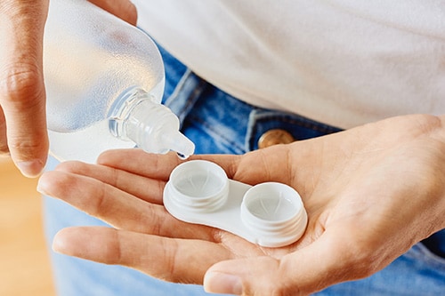 Person putting solution into contact lens case