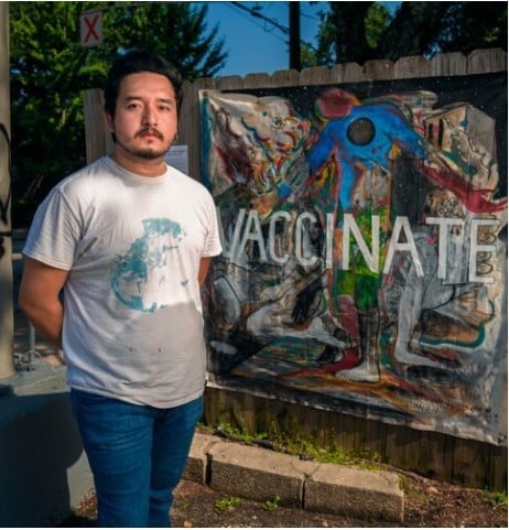 Photo of artist Sergio Suarez, standing in front of his artwork.