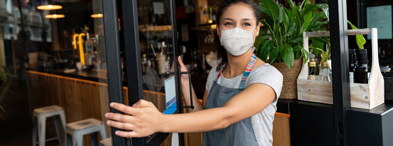 Young woman opening a coffee shop door with mask on