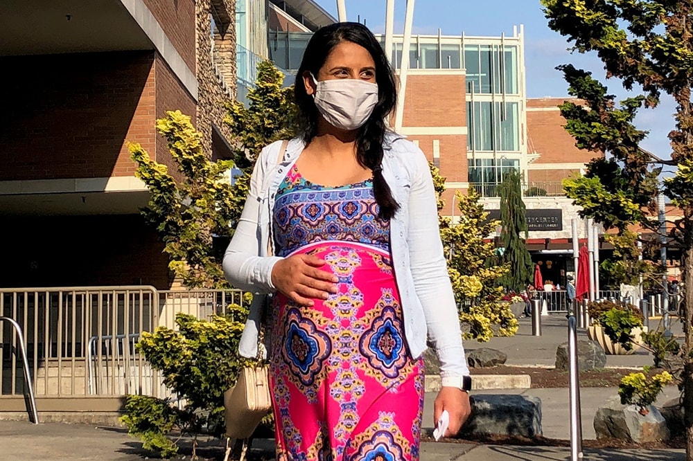 一名戴着布制防护口罩的孕妇在城市中行走