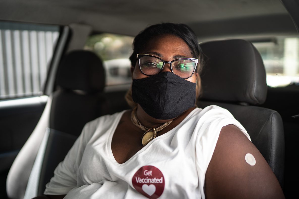 一名开心的女性坐在车里，戴着口罩，贴着“接种疫苗”的贴纸的半身像